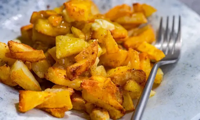 Un plato de patatas asadas doradas y crujientes, sazonadas con hierbas y especias, listas para ser disfrutadas con un tenedor.