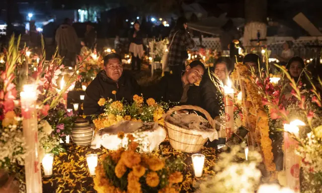 Rodzina przy grobie ozdobionym świecami i kwiatami na Dia de los Muertos.