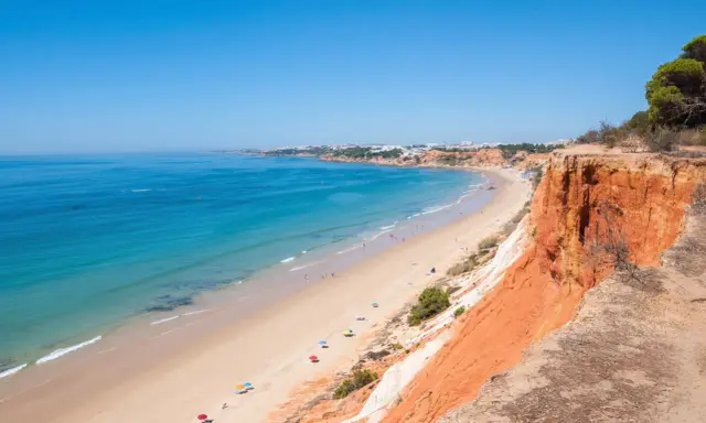 Blick auf den Strand Praia da Falésia mit seinen roten Felsen und der Stadt im Hintergrund.
