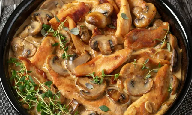 Pyszne polędwiczki z kurczaka w kremowym sosie z pieczarkami, udekorowane świeżym tymiankiem.