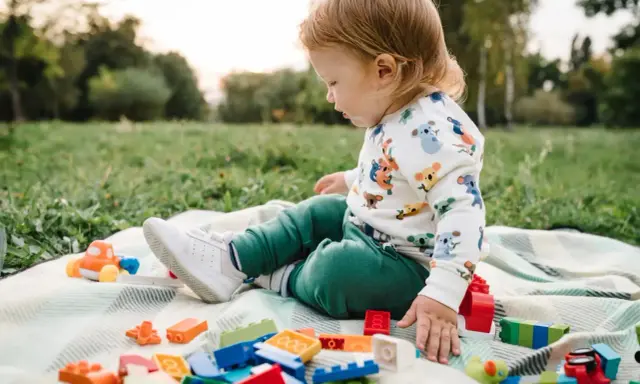 Un niño pequeño juega con bloques de construcción y un coche de juguete en el césped, disfrutando de actividades para niños de 2 a 3 años.
