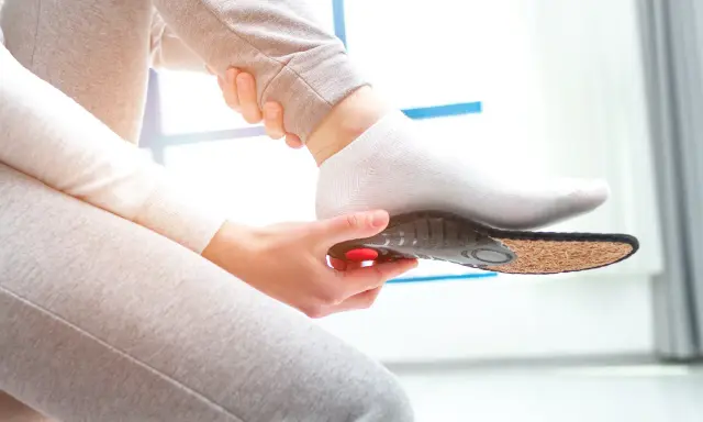 Une personne insère une semelle orthopédique dans sa chaussette. Une solution pour une pedicure remboursé.