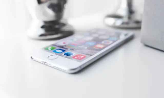 Biały iPhone leży na białym blacie, gotowy do pracy. W tle widać błyszczące i matowe elementy dekoracyjne.