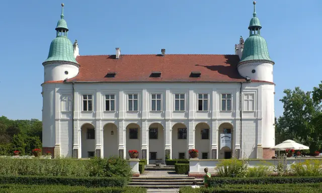 Baranów Sandomierski atrakcje: Zamek z arkadowym podcieniem i zielonymi wieżyczkami, otoczony zadbanym ogrodem.