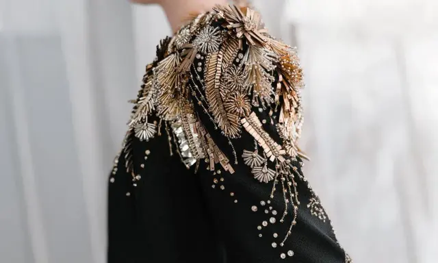 A black garment with an elaborate shoulder embellishment of gold and silver beads, sequins, and crystals, showcasing the definition of embellished fashion.