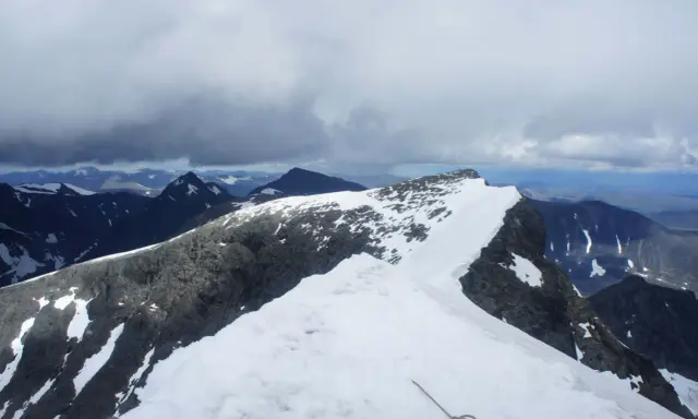 Snöklädda bergstoppar och molniga himlar. En repstump syns i förgrunden, redo för äventyret på Kebnekaise leder.