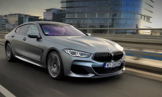 Srebrne BMW M850i sunie po moście, odbijając światła miasta w swoich szybach.