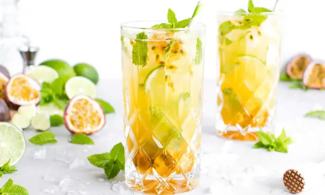 Zwei erfrischende Passion Fruit Mojitos mit Minze und Limette, umgeben von frischen Früchten und Eis.