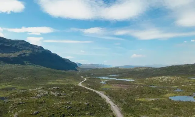 Väg slingrar sig genom ett vidsträckt landskap med berg och sjöar. Perfekt för camping i Norrbotten.