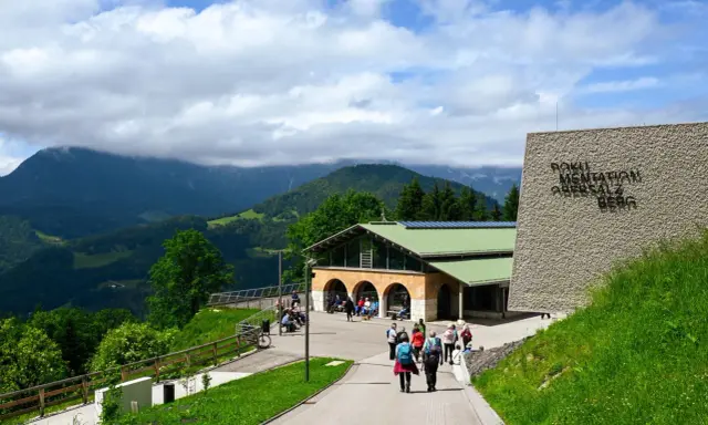 Besucher erkunden das Dokumentationszentrum Obersalzberg, umgeben von grünen Hügeln und Bergen.