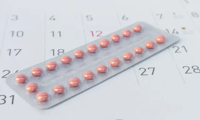 Różne rodzaje tabletek antykoncepcyjnych w blistrze na tle kalendarza.
