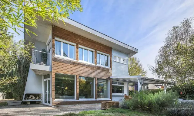 Architecture maison année 60 avec bardage bois et grandes baies vitrées, balcon moderne, entourée de verdure.