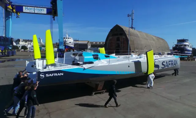 Équipe poussant un **60 pieds IMOCA** de course au large, le Safran, dans un chantier naval.