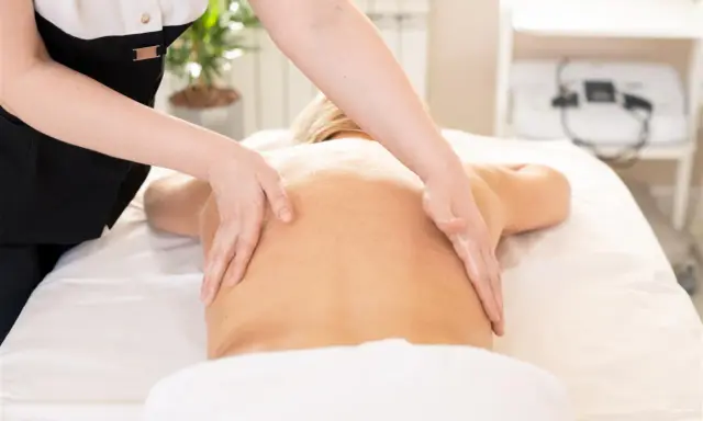 Relaksacyjny masaż kręgosłupa wykonany dłońmi terapeuty. Skóra lśni od olejku, a ruchy dłoni przynoszą ulgę.