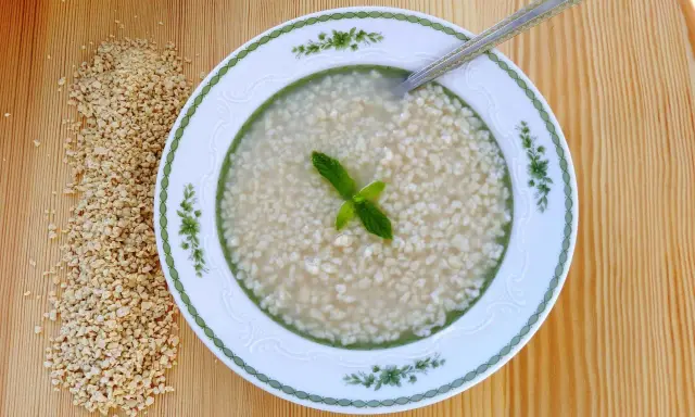 Eine Schüssel mit Trahana, garniert mit Minze, neben einem Haufen getrockneter Trahana. Ein Löffel liegt in der Schüssel.