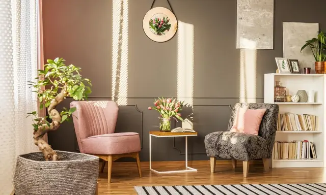 Un angolo relax casa con due poltrone, un tavolino con fiori e libri, e una libreria. Luce solare crea un'atmosfera accogliente.