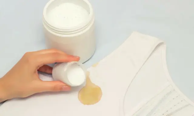 Mano aplica polvo blanqueador sobre mancha amarilla en ropa blanca. ¡Descubre cómo blanquear ropa blanca fácilmente!