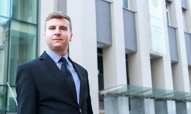 Mężczyzna w garniturze przed budynkiem sądu.