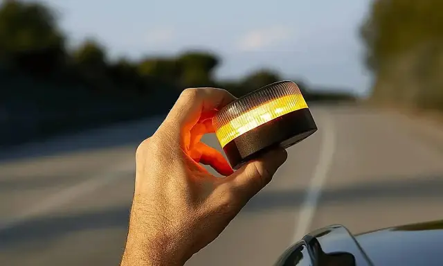 Mano sujeta una baliza de emergencia naranja brillante, lista para evitar una multa o señalizar un peligro en la carretera.