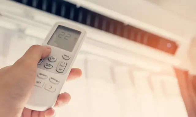 Mano ajustando el control remoto del aire acondicionado a 22 grados. ¿Cuántas frigorías por metro cuadrado necesita tu hogar para estar fresco?