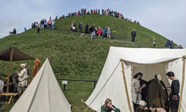 Ludzie wchodzą na Kopiec Kraka, a u jego podnóża rozstawiono historyczne namioty.