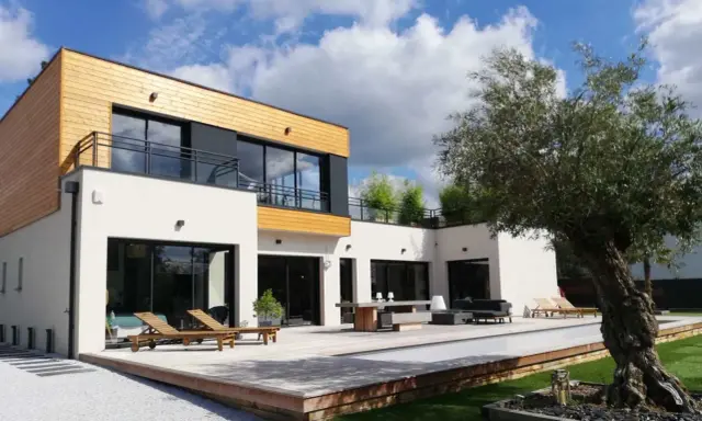 Maison moderne avec un style architectural audacieux, mêlant bois et blanc. Terrasse spacieuse avec mobilier extérieur et piscine.