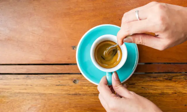 Mani che mescolano un caffè, nonostante si dica che il caffè è cancerogeno, il suo aroma attira.