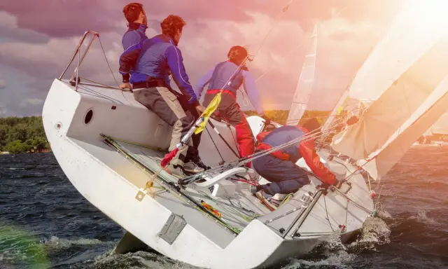 Équipe en pleine action pour apprendre la voile. Le voilier est incliné, les marins ajustent les voiles sous un ciel orageux.