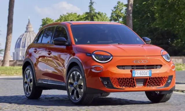 El nuevo Fiat 600, un SUV naranja vibrante, se exhibe con elegancia frente a la cúpula de San Pedro en Roma.