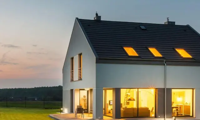 Une maison moderne et lumineuse, une maison autonome en France, avec de grandes fenêtres éclairées par une lumière chaude.