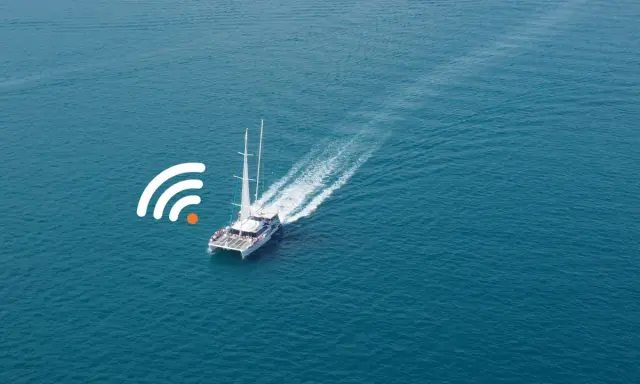 Un catamaran à voile navigue sur une mer bleue, avec un symbole de connexion Wi-Fi à proximité.