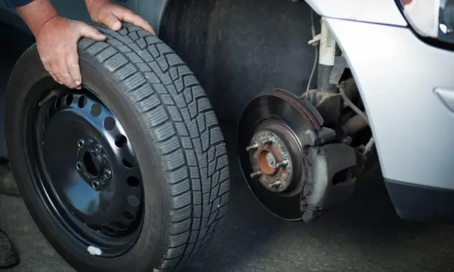 Mani che cambiano una gomma invernale, rispettando l'obbligo cambio gomme per la sicurezza stradale.