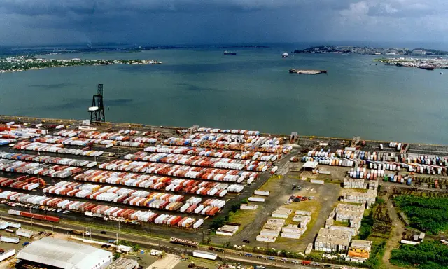 Vasto deposito di container nel porto di San Juan, Porto Rico, con navi in lontananza sotto un cielo nuvoloso.