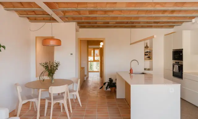 Comedor y cocina luminosos en una casa vieja decorada con poco dinero. Techos de vigas de madera y baldosas de terracota.