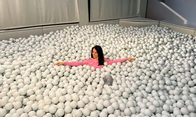 Mujer sonriente se sumerge en una piscina de bolas blancas, un divertido ikono madrid.