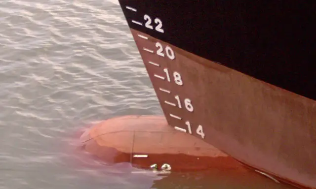 La coque d'un navire, marquée de -22 à -14, flotte sur l'eau. Le déplacement léger du bateau est visible.