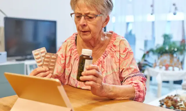Starsza pani z tabletką w ręku sprawdza zwrot za leki dla seniorów.