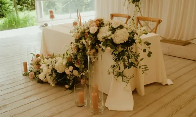 Elegancki stół pary młodej ozdobiony bujną wiązanką kwiatów i świecami.