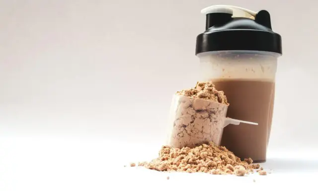 Ein Löffel Proteinpulver neben einem fertigen Proteinshake im Shaker. Perfekt für den proteinreichen Start in den Morgen.