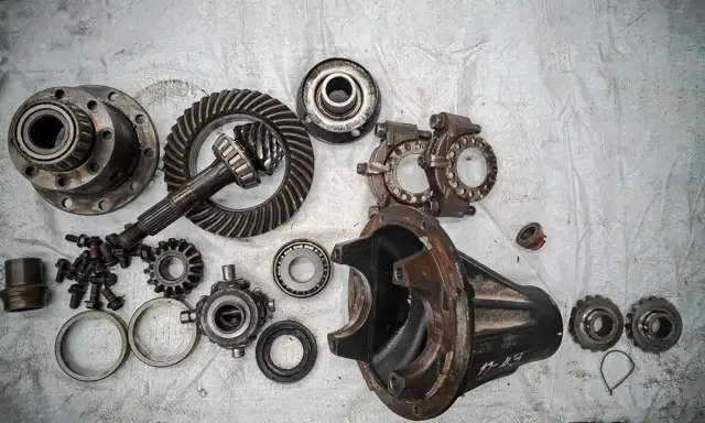 Rozłożony mechanizm różnicowy w skrzyni biegów: koła zębate, wałek atakujący, obudowa i łożyska.