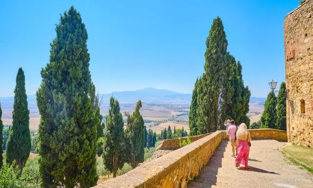 Coppia in cammino durante un tour Toscana 5 giorni, tra cipressi e colline ondulate sotto un cielo azzurro.