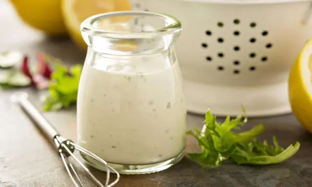 Ein Glas cremiges Ranch Dressing, daneben ein Schneebesen, Salatblätter und Zitronenspalten. Perfekt für dein Ranch Dressing Rezept!