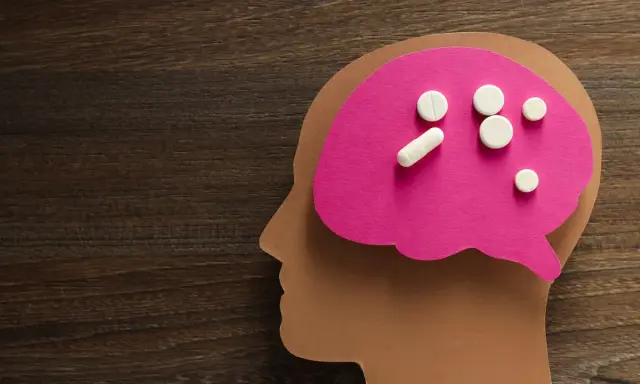 Papierowy profil głowy z różowym mózgiem, na którym leżą tabletki. Symbolizują one psychobiotyki na depresję, szukając ulgi dla umysłu.