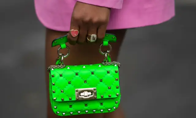 Borsa verde neon, colore complementare del fucsia, con borchie dorate e catena. Indossata da una mano con anelli.
