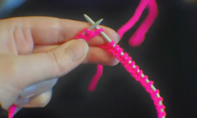 En hand håller stickor och ljusrosa garn, redo att starta stickning.