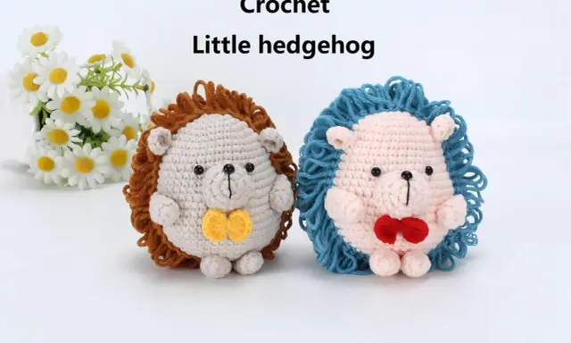Dos adorables erizos de crochet, uno beige con pajarita amarilla y otro rosa con pajarita roja, posan junto a un ramo de margaritas.