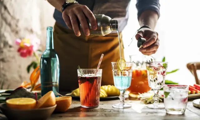 Barman przelewa płyn z shakera do drinka, tworząc kolorowe koktajle. Mieszanie alkoholi to sztuka.