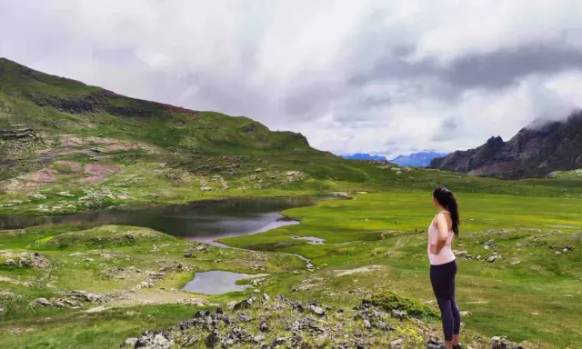 Mujer admira un lago y prados verdes en el Valle de Tena, ideal para rutas de senderismo.