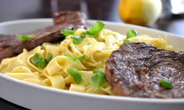 En krämig pastarätt med tagliatelle, garnerad med färsk basilika och serverad med saftig entrecote.