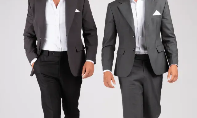 Two men in suits. The one on the left wears a dark grey sport coat with black pants. The one on the right wears a medium grey suit. Both are dressed for a wedding.